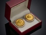 une paire de boutons de manchette plaqués or, présentés dans un coffret rouge posé sur un fond noir