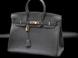 a black leather handbag with gold hardware on a black background