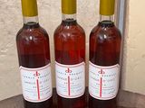 three bottles of wine sitting on top of a barrel next to a wall