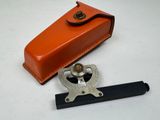 un étui en cuir orange sur lequel figurent une boussole et une règle, posés sur une surface blanche