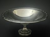 un plat ancien en argent posé sur un socle, sur fond noir