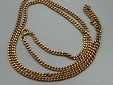 un collier à chaîne en or posé sur une surface grise