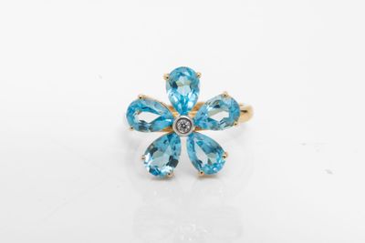 une photo d'une bague ornée d'une fleur en topaze bleue, posée sur une surface blanche