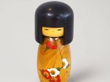 une petite poupée en bois aux cheveux noirs, vêtue d'un kimono jaune