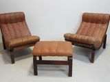 two brown leather chairs and a foot stool in a white room