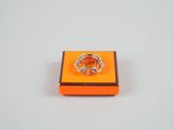 une boîte orange surmontée d'un anneau, posée sur une surface blanche