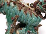 a statue of a dragon on a pedestal with a clock in the background