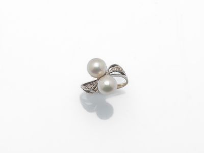 une bague en perle blanche et diamants posée sur une surface blanche