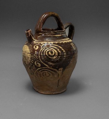 an old brown vase with a handle sitting on a gray surface