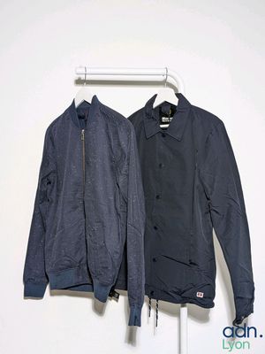 two jackets hanging on a clothes rack against a white wall