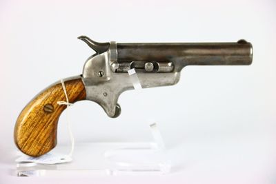 un vieux pistolet avec une crosse en bois, posé sur un socle transparent