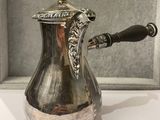 a silver coffee pot with a handle on a table