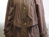 manteau marron à col en fourrure posé sur un mannequin devant un mur blanc