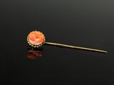 une broche aux couleurs or et corail, posée sur un fond noir