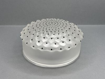 un vase blanc parsemé de points noirs, posé sur un fond gris