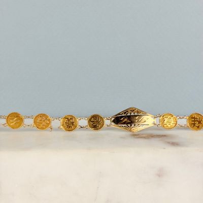 un gros plan d'un bracelet en or orné de pièces de monnaie, posé sur une surface en marbre