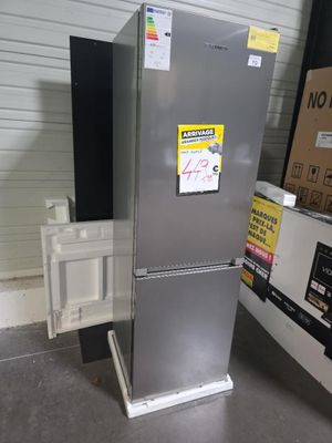 un réfrigérateur argenté posé dans un entrepôt, avec des cartons par terre