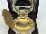 miroir de poche plaqué or dans un écrin bleu posé sur une surface blanche
