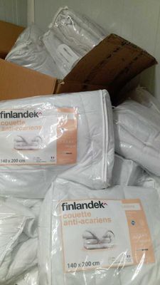 Des cartons contenant de la literie sont empilés les uns sur les autres dans une pièce.