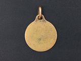 a gold plated pendant with a small disc on a black background