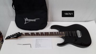 une guitare électrique noire posée sur une table blanche, à côté d'un sac noir