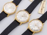 three gold tone watches with black leather straps and tags
