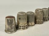 several silver thimbles lined up in a row on a white surface