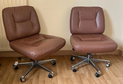 une paire de fauteuils de bureau en cuir marron posés sur un parquet en bois massif