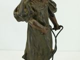 statue en bronze représentant une femme tenant un fouet, posée sur un socle en bois
