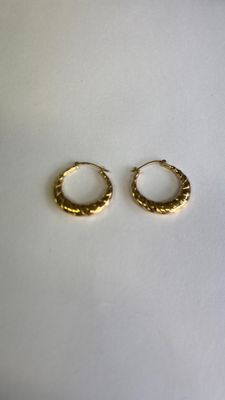deux petites boucles d'oreilles en or en forme d'anneau sur une surface blanche