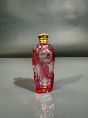 a red glass bottle with a gold lid sitting on a table