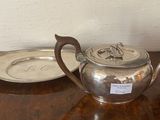 a silver tea pot on a wooden table with a silver plate