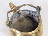 a small brass pot with a handle on a white surface