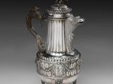 une cafetière en argent avec une anse en forme de dragon, posée sur un socle