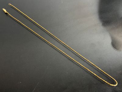 a gold necklace with a long chain on a black surface