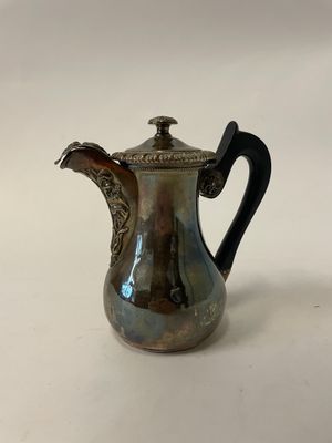 une cafetière ancienne en argent avec une poignée noire sur une surface blanche