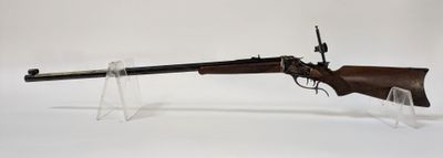 un vieux fusil au canon en bois, posé sur un socle en acrylique transparent