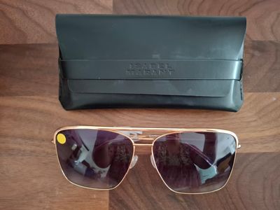 des lunettes de soleil et leur étui posés sur une table en bois, à côté d'un sac noir