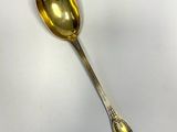 une cuillère en argent avec un manche en or, posée sur une surface blanche