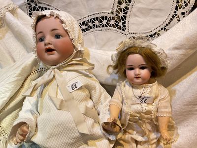 deux poupées assises l'une à côté de l'autre sur un lit