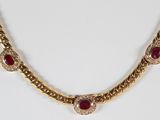 a close up of a gold necklace with red stones on it
