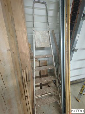 une échelle appuyée contre un mur, à côté d'un tas de bois