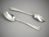 two silver spoons sitting on top of a table next to each other