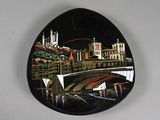 a black oval plate with a picture of a bridge and buildings on it