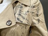 an image of a mannequin dressed in a trench coat with paint splattered on it