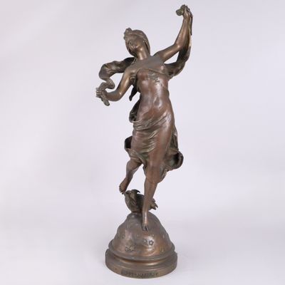 une statue antique en bronze représentant une femme tenant un oiseau, posée sur un socle