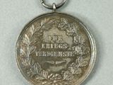 an old silver medal with a wreath on it on a white surface