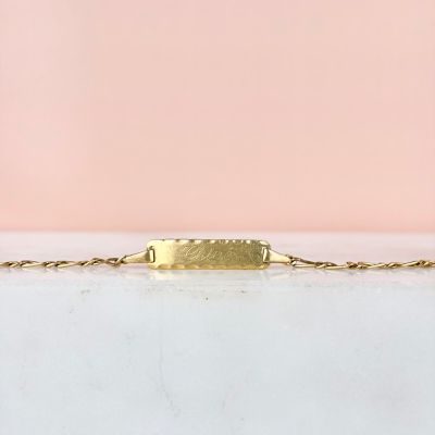 un bracelet en or avec une barre suspendue à une chaîne, sur fond rose
