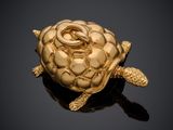 une image représentant une broche en forme de tortue dorée posée sur une surface noire