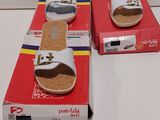 une paire de sandales blanches pour femme, dans une boîte posée sur une surface blanche